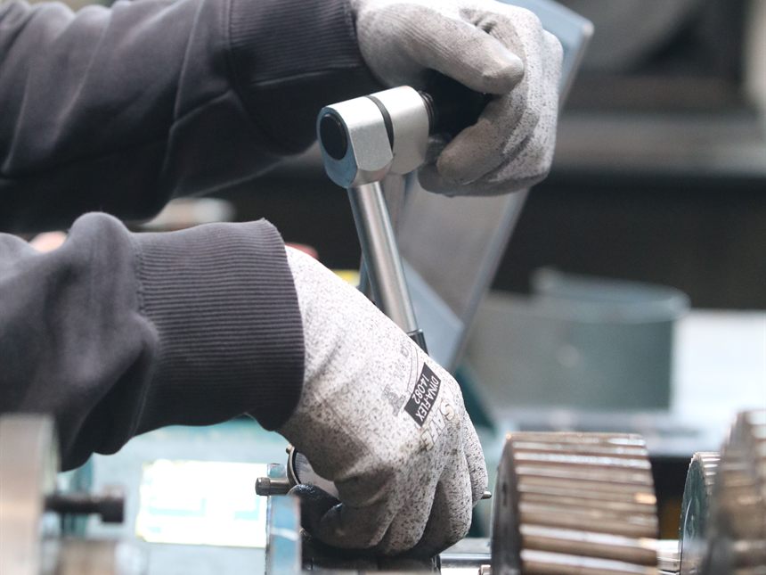 En atelier, deux mains gantées serrent une pièce à la clé dynamométrique sur une boîte de vitesses démontée