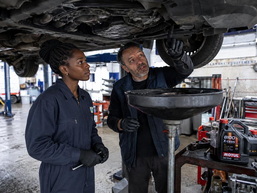 Un tuteur et une alternante en mécanique automobile sous un véhicule sur pont, en atelier